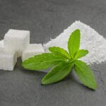 Zuckerwürfel und Stevia-Blätter auf schwarzem Untergrund