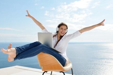 Frau mit Laptop und Kopfhörern am Meer