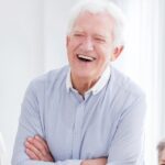 Lächelnder älterer Mann in grauem Hemd.