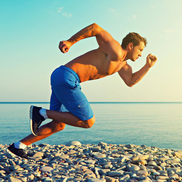 Durchtrainierter Mann in kurzer blauer Hose sprintet auf Steinbett nahe dem Meer.