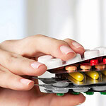 Hand hält Tablettenpackungen vor dem Mund.