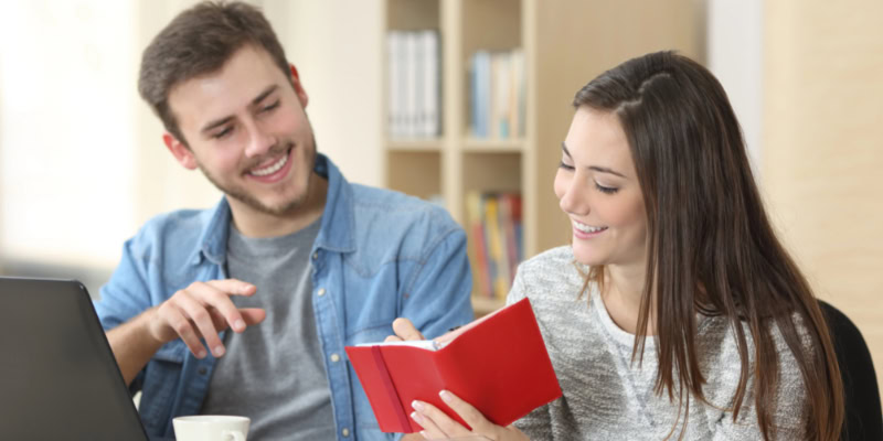 Junges Paar lernt mit Laptop und rotem Buch